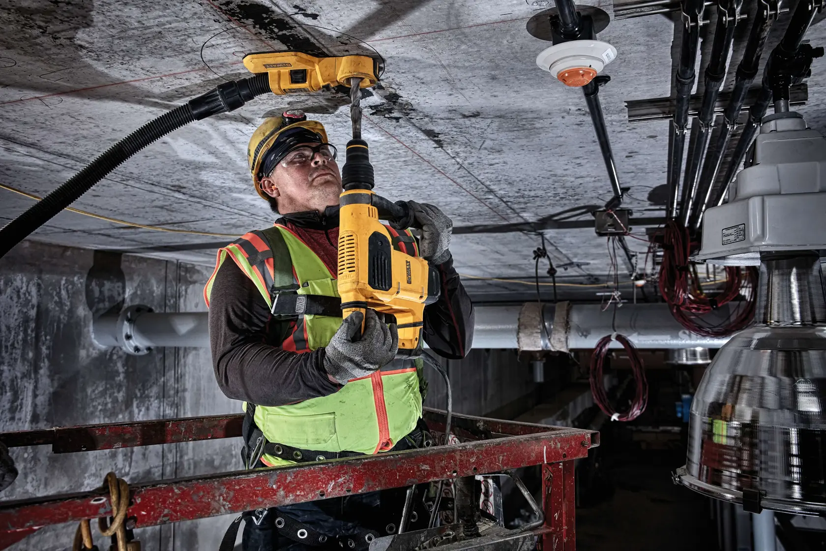 Trabalhador usa furadeira DEWALT no teto, veste colete de alta visibilidade e equipamento de segurança.