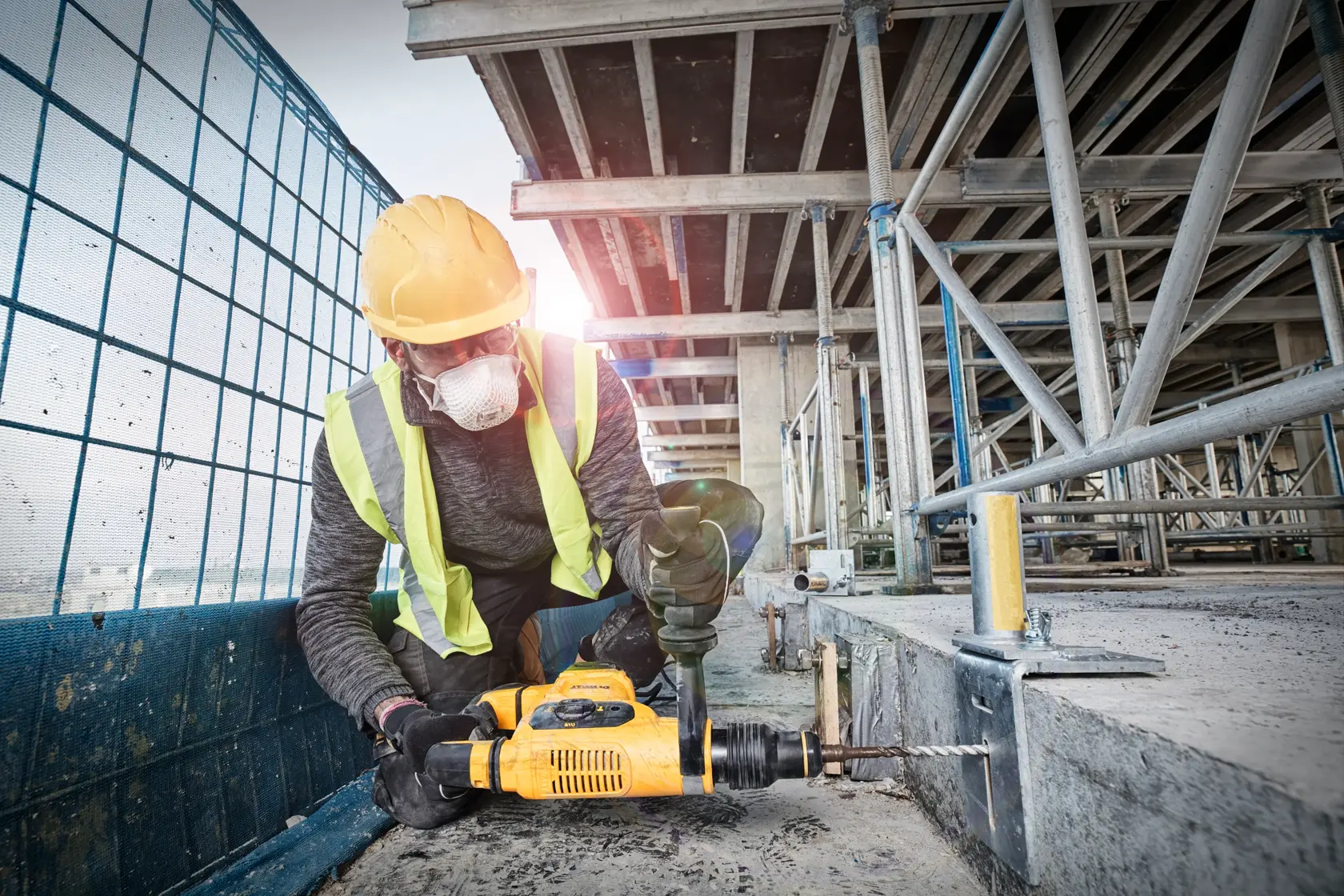 Um trabalhador da construção civil, usando capacete amarelo e colete refletivo, está usando um martelete amarelo DEWALT para perfurar uma superfície de concreto em um canteiro de obras.