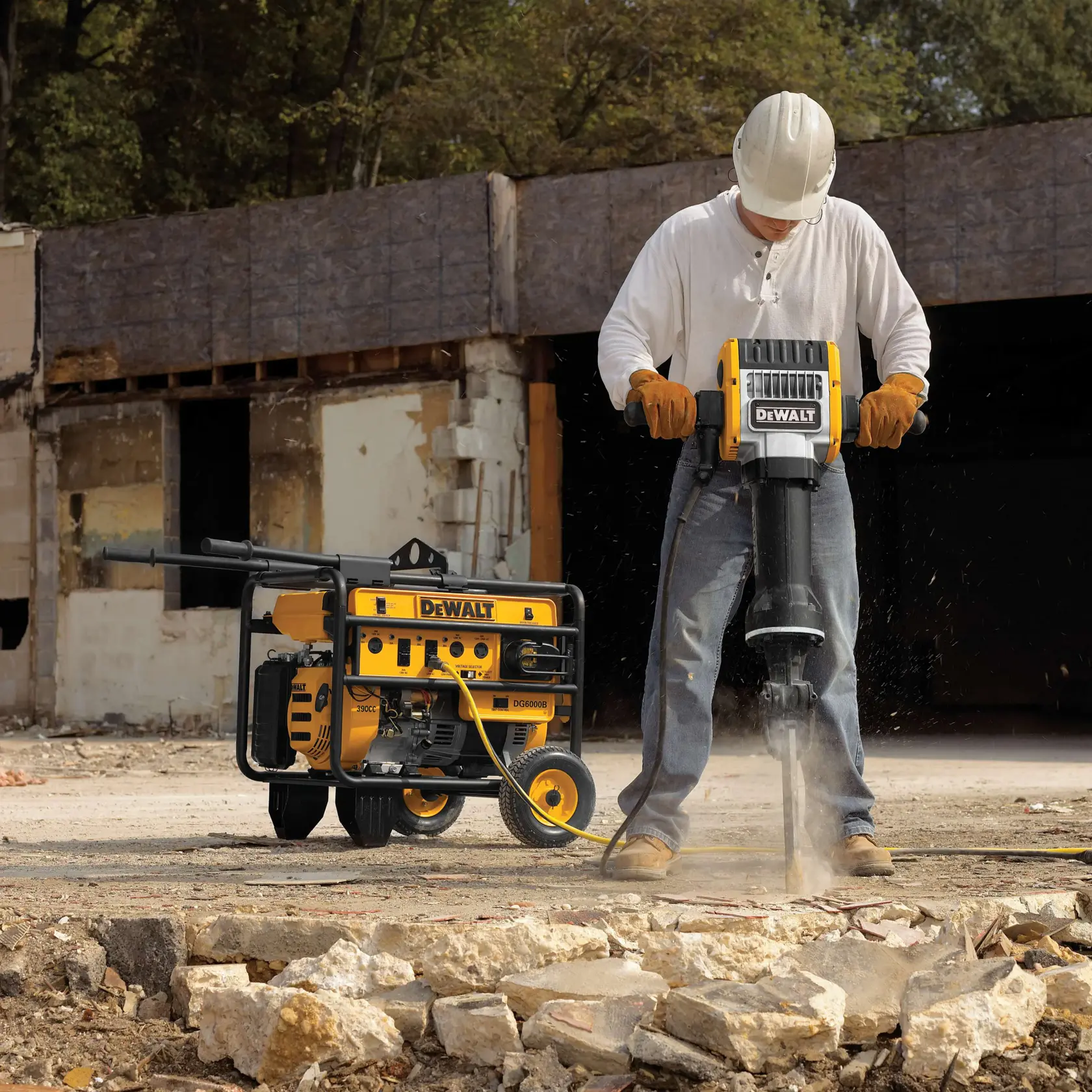 Um trabalhador da construção civil usando capacete, luvas e botas opera um martelete DEWALT quebrando concreto, com um gerador DEWALT ao fundo em um local de demolição ao ar livre.