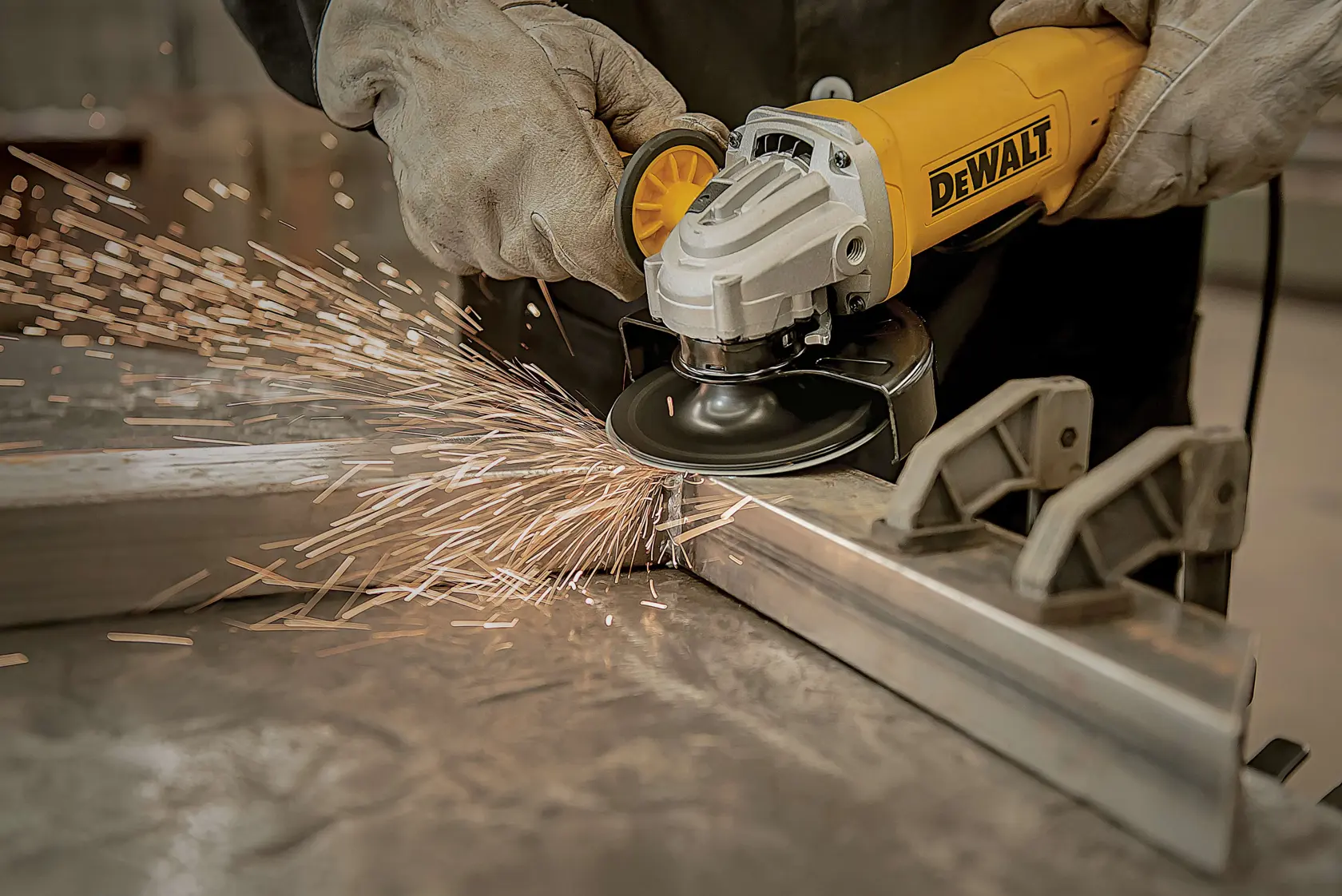 Uma pessoa usando luvas utiliza uma esmerilhadeira angular amarela DEWALT para cortar ou lixar uma peça de metal, produzindo faíscas.