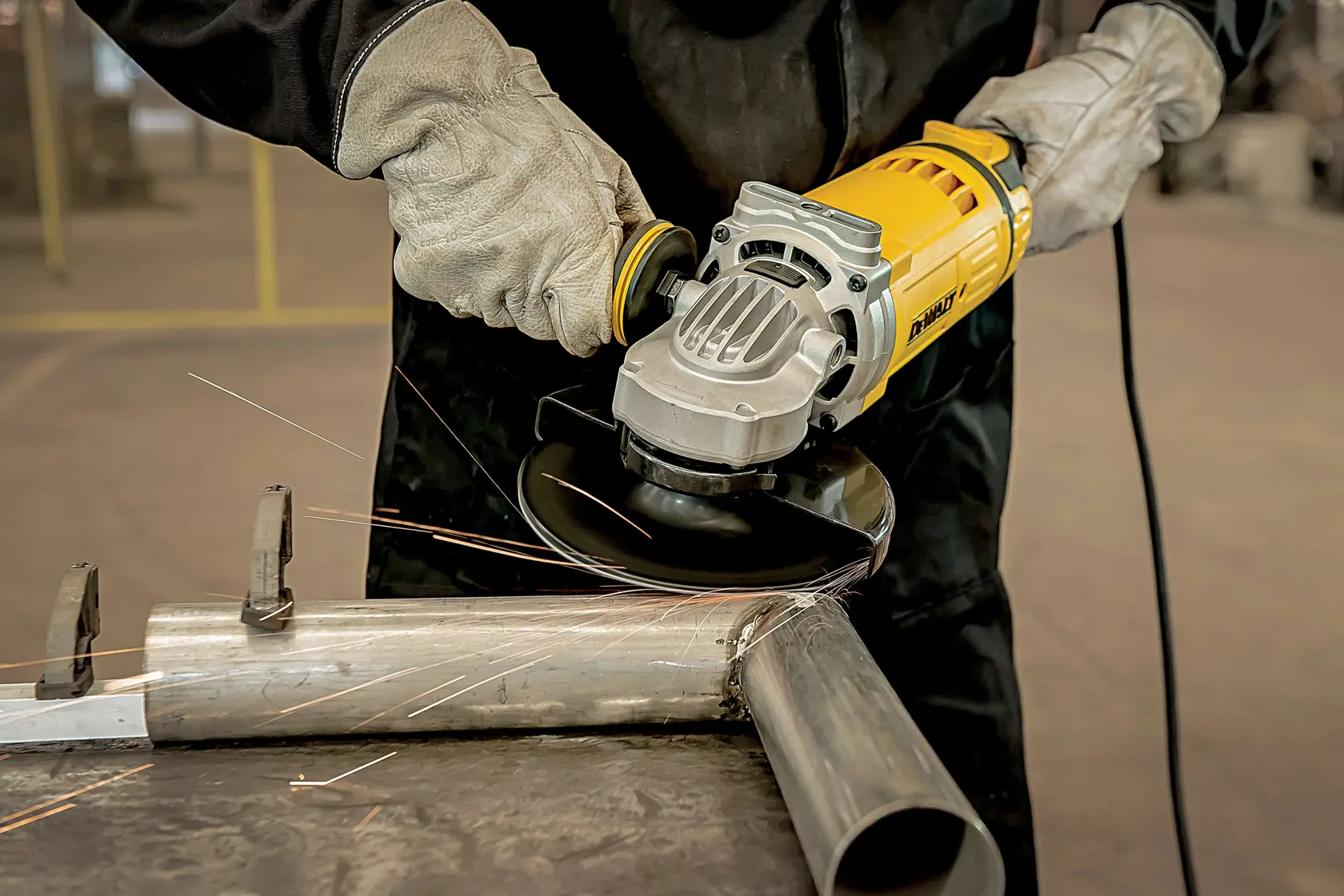 Uma pessoa usando luvas de proteção utiliza uma esmerilhadeira amarela DEWALT para lixar um tubo de metal, gerando faíscas.