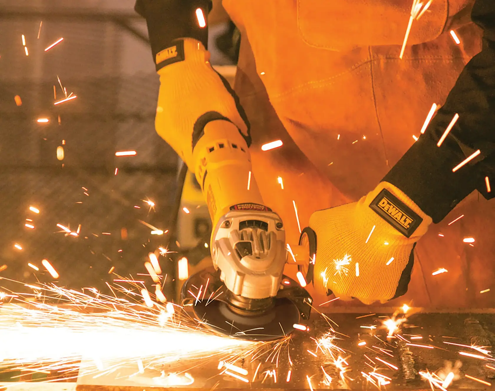 Pessoa usando luvas amarelas e roupa de proteção opera uma esmerilhadeira angular DEWALT, criando faíscas brilhantes ao lixar metal.