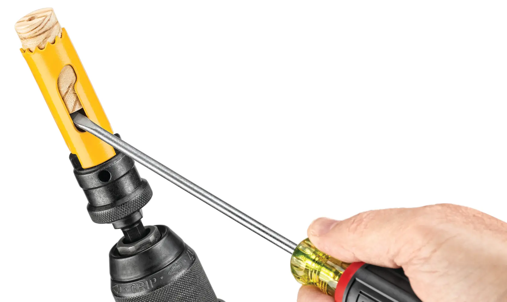 Uma visão aproximada de uma pessoa usando uma chave de fenda para remover um pedaço de madeira preso dentro de uma serra copo amarela acoplada a uma furadeira.