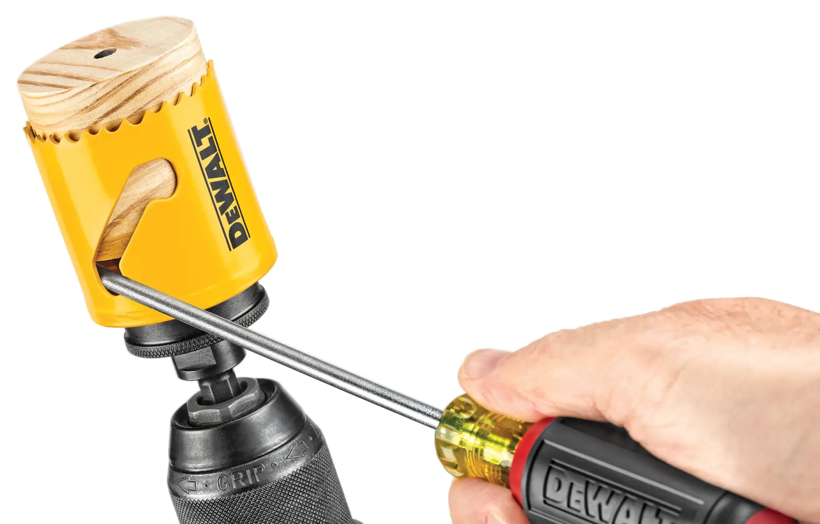 Close-up de uma serra copo amarela da DEWALT acoplada a uma furadeira, com uma mão usando uma chave de fenda para remover um plugue de madeira de dentro da serra copo.