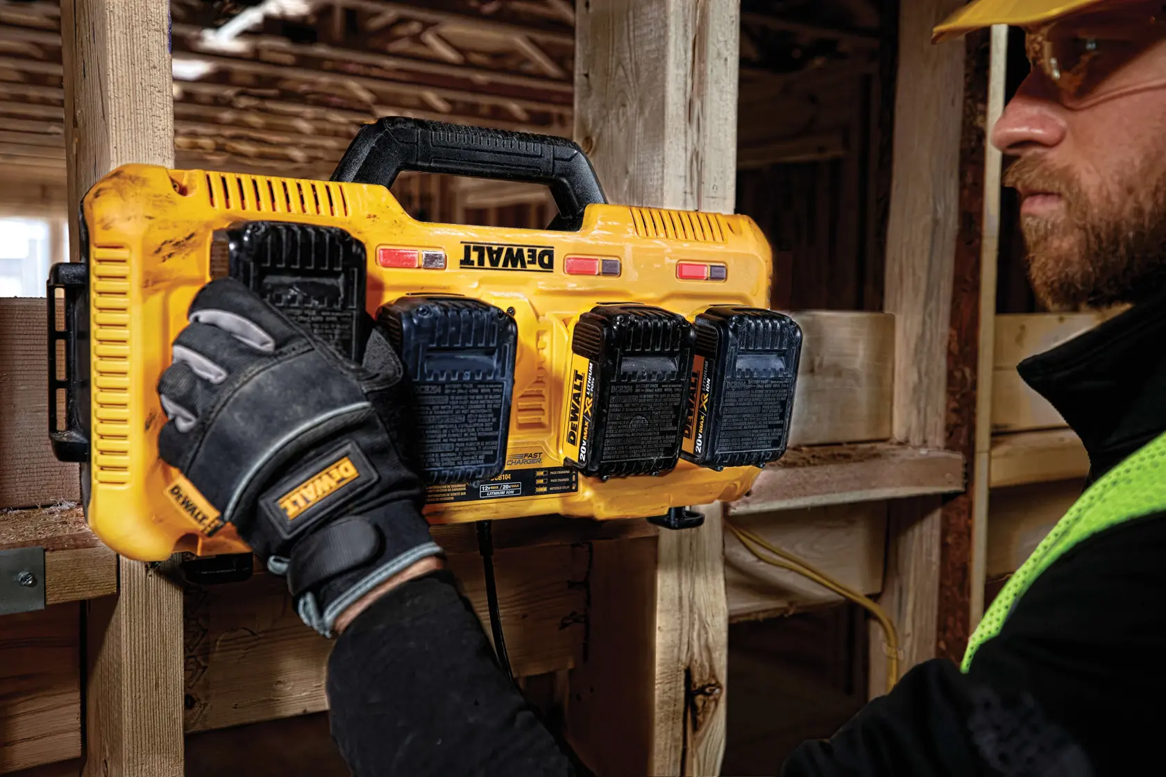 Un cargador de baterías portátil amarillo DEWALT DCB104 con cuatro ranuras de carga y un asa negra, diseñado para baterías de herramientas eléctricas.