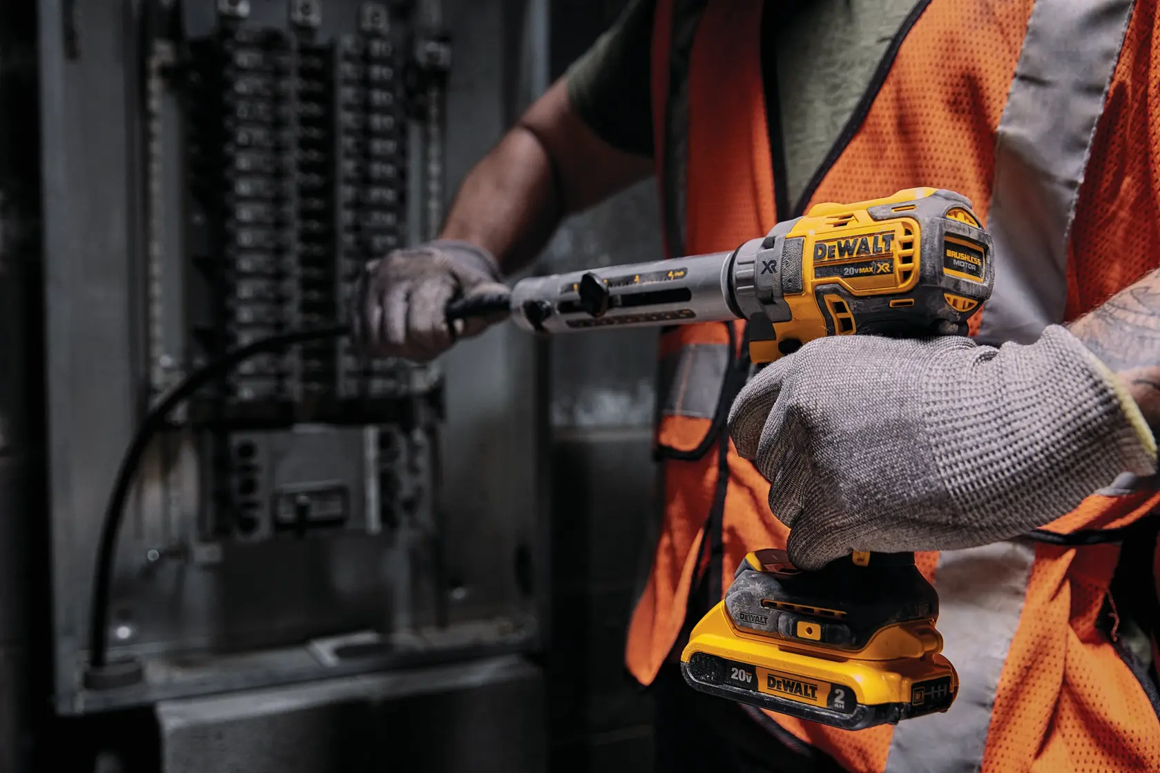 Trabalhador usa ferramenta DEWALT 20V perto de painel elétrico, com luvas e colete de segurança laranja.