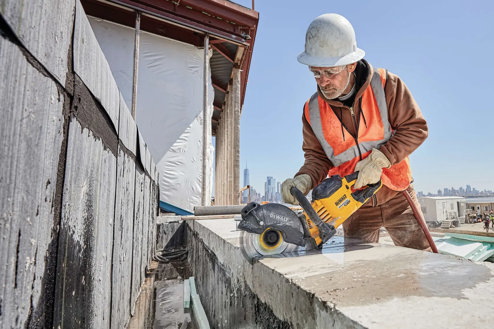 Foto de trabalhador cortando concreto com serra DEWALT alimentada por bateria DCB609 em obra.