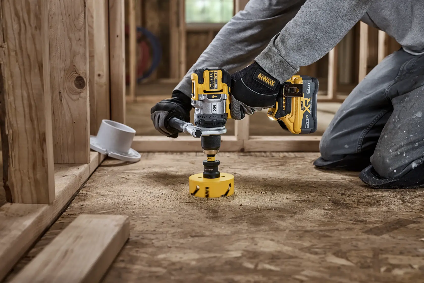 Mão com luva usando uma furadeira DEWALT sem fio no chão de obra, com ferramentas e parafusos próximos.