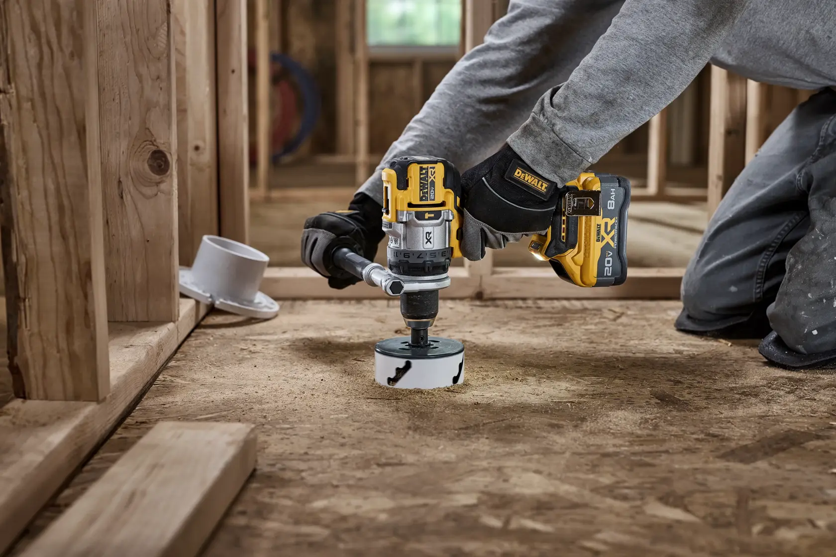 Pessoa usa furadeira DEWALT sem fio com serra copo em piso de madeira em obra.