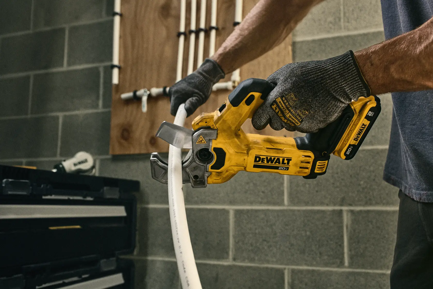 Close-up de uma ferramenta elétrica portátil DEWALT cortando um tubo de plástico branco sobre uma bancada. A ferramenta é amarela e prateada, com aparas de plástico visíveis na superfície.