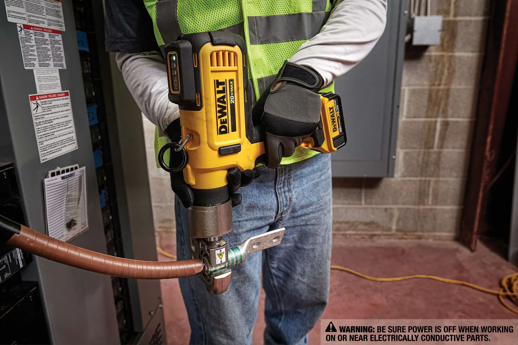 Uma pessoa usando luvas de trabalho e colete de segurança está utilizando uma ferramenta de crimpagem sem fio DEWALT para crimpar um cabo de cobre. O texto na imagem diz: '750 MCM CU / 750 AI Capacidade de crimpagem para cabo de cobre e alumínio.'