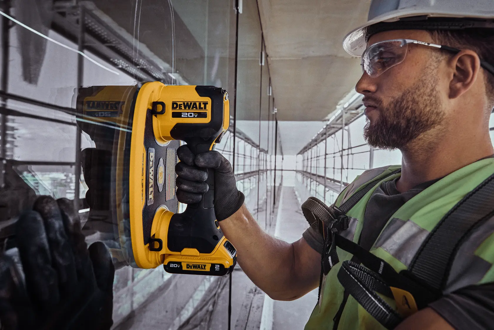 Um trabalhador usando calças marrons e luvas de proteção utiliza uma ferramenta portátil DEWALT em uma grande chapa de OSB em um canteiro de obras. O trabalhador possui um cinto de ferramentas com várias ferramentas manuais.