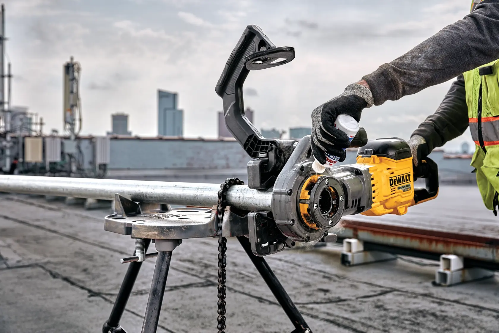 Um trabalhador usa uma máquina de roscar tubos elétrica DEWALT para roscar um tubo de metal fixado em um tripé em um local industrial ao ar livre.