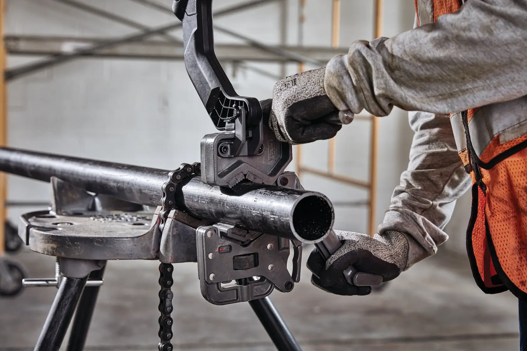 Um trabalhador usando luvas e colete de segurança laranja opera uma ferramenta de corte de tubos DEWALT presa a um tubo de metal em um ambiente industrial interno.