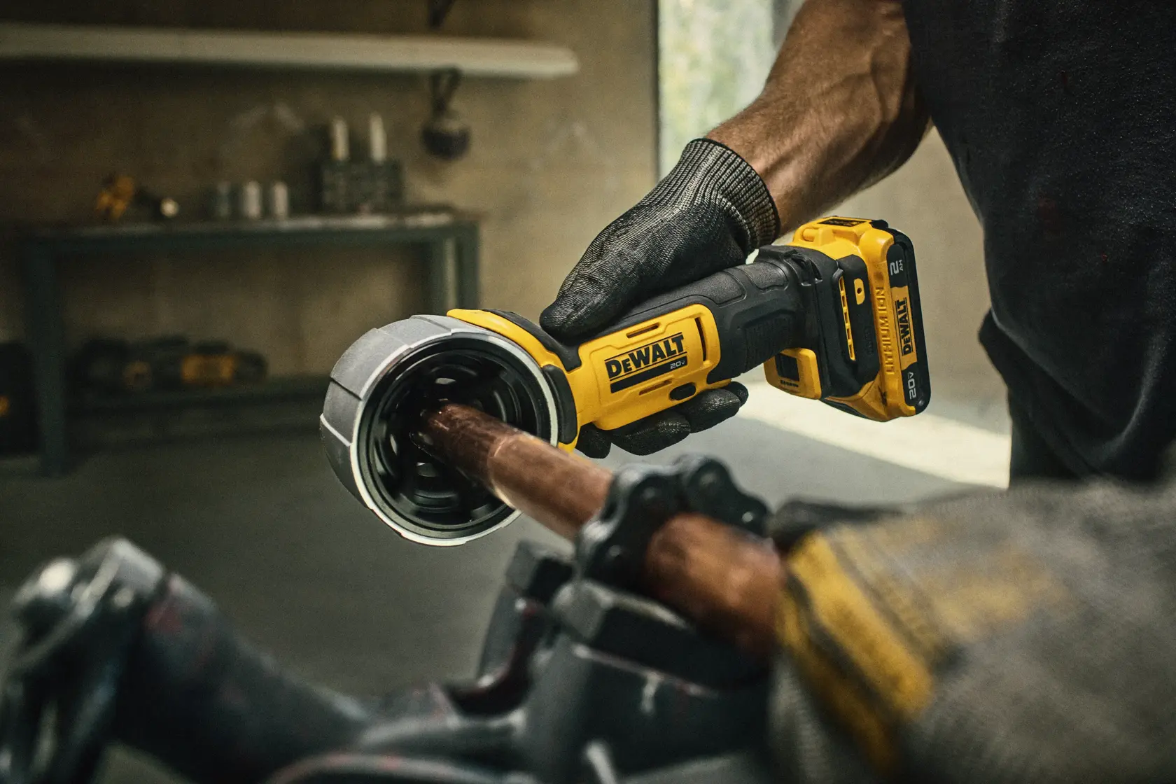 Uma ferramenta elétrica sem fio DEWALT é segurada por uma pessoa usando luvas de trabalho, cortando um tubo de metal. O texto abaixo destaca que a ferramenta pode ser usada com mais de 60% tipos de materiais a mais. A bateria é vendida separadamente.