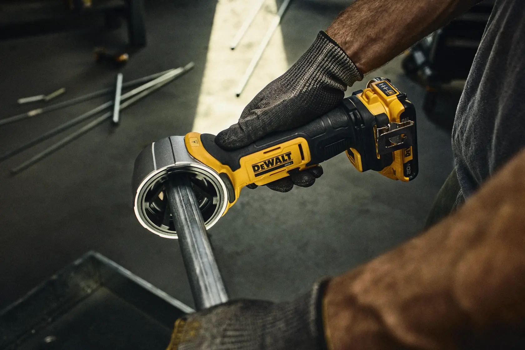 Uma pessoa usando luvas utiliza um cortador de tubos sem fio DEWALT 20V para cortar um tubo de plástico branco em uma oficina. A ferramenta corta o tubo, e o texto indica que pode cortar tubos com 33% de diâmetro maior em comparação com um modelo especificado. 'Bateria vendida separadamente' é mencionado na imagem.