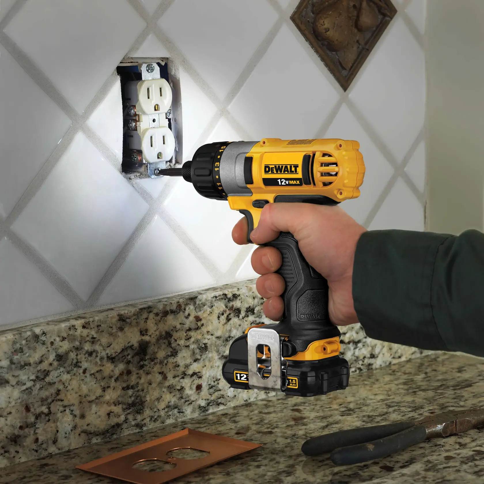 Uma pessoa utiliza uma furadeira sem fio amarela DEWALT 12V MAX para instalar ou remover parafusos de uma tomada elétrica de parede, com a furadeira posicionada próxima a um backsplash de azulejo e uma bancada de granito.