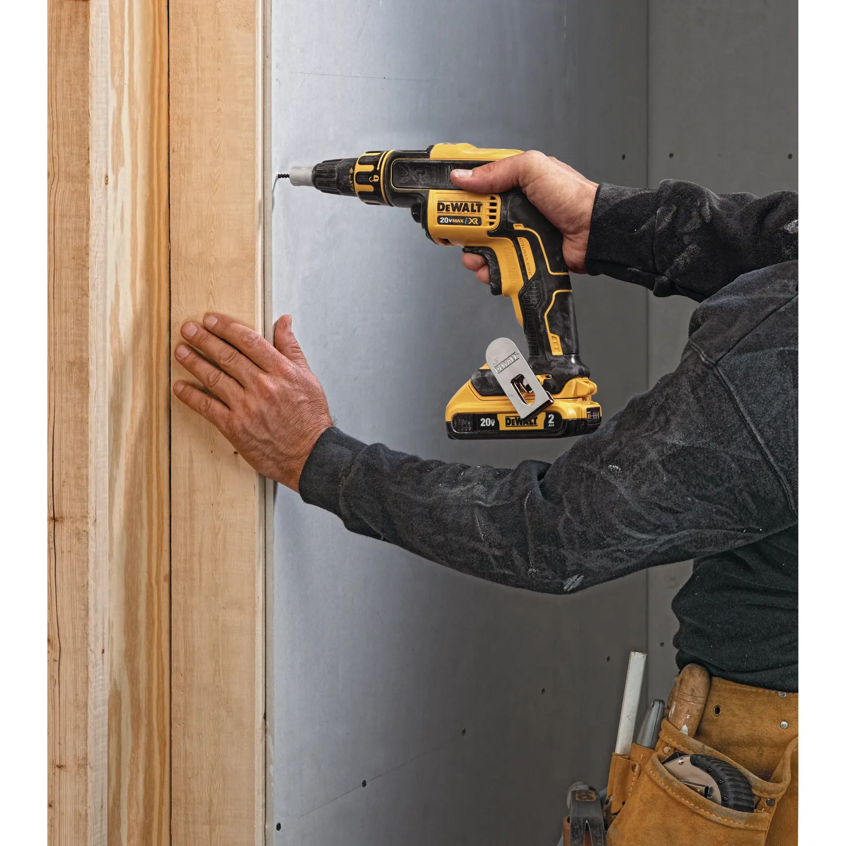 Uma pessoa utiliza uma parafusadeira sem fio DEWALT 20V MAX XR para fixar drywall em uma estrutura de madeira. A ferramenta é amarela e preta, e a pessoa está usando cinto de ferramentas e roupas de trabalho.