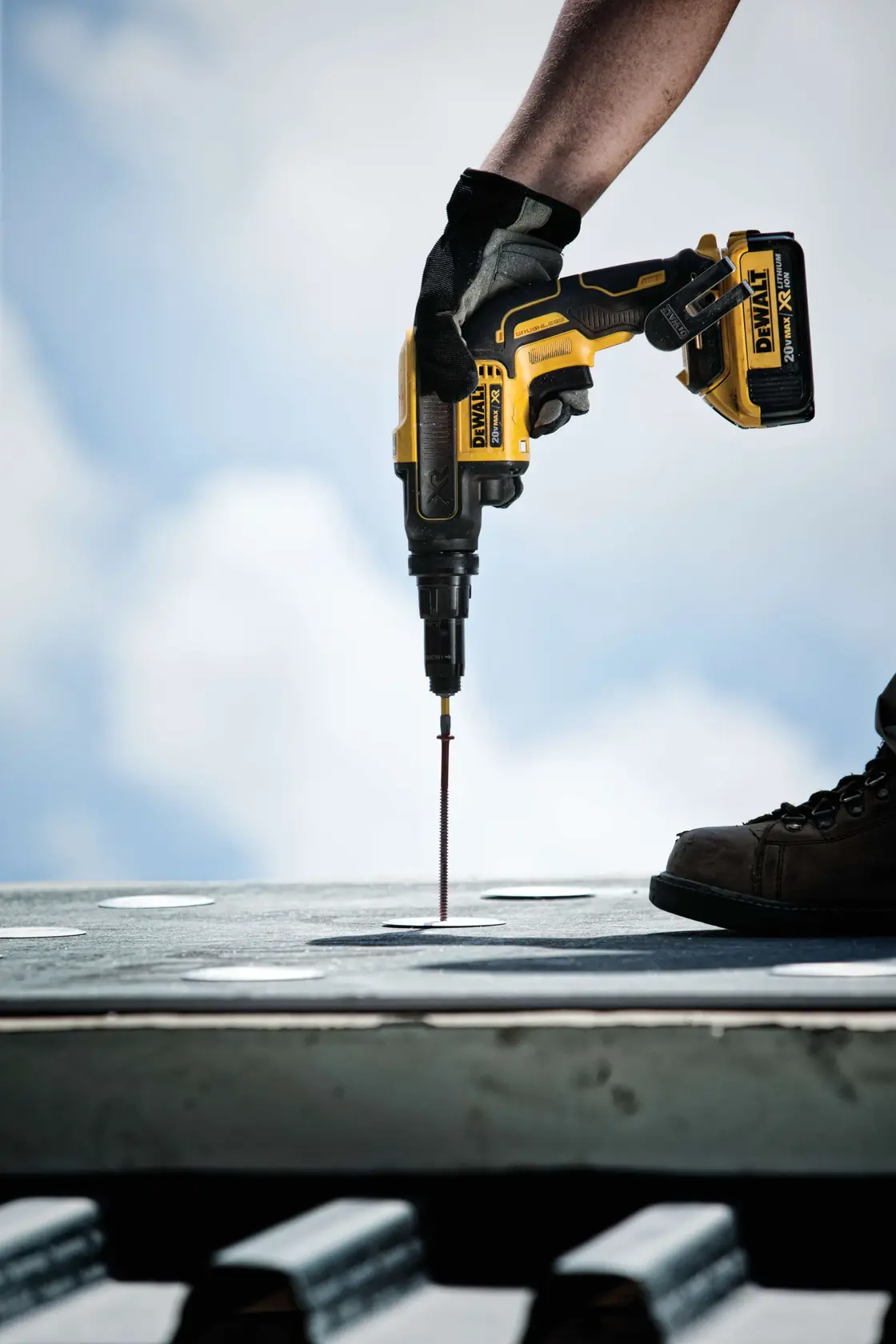 Uma pessoa usando luvas e óculos de proteção utiliza uma ferramenta elétrica sem fio DEWALT para trabalhar em uma folha de metal em uma oficina industrial.