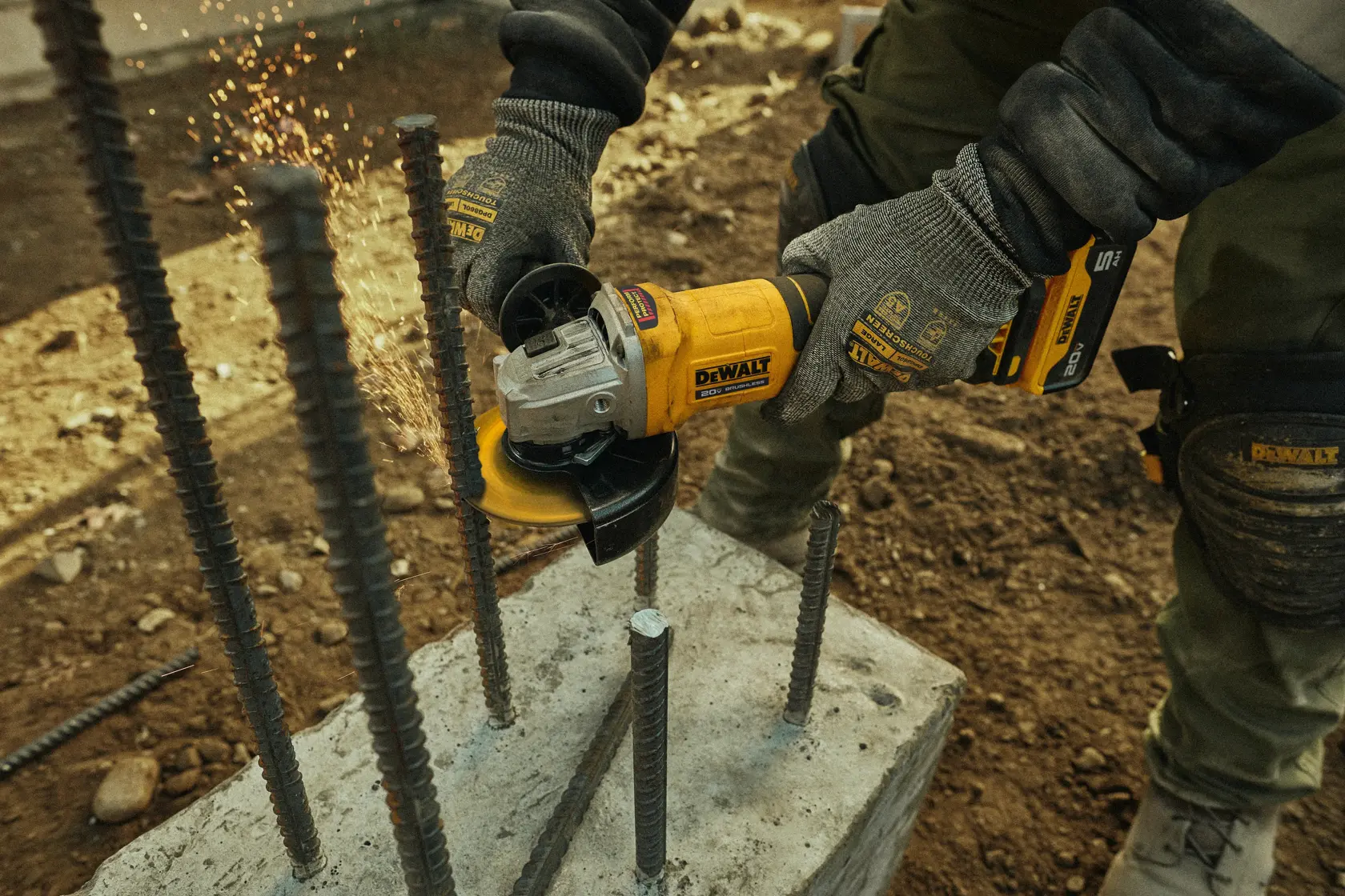 Uma pessoa usando luvas utiliza uma esmerilhadeira angular sem fio DEWALT 20V para cortar vergalhão, produzindo faíscas. O texto destaca que a ferramenta pode fazer até 56 cortes de vergalhão de 1/2 polegada por carga, usando bateria DCB205 e disco de corte DW8062, vendidos separadamente.