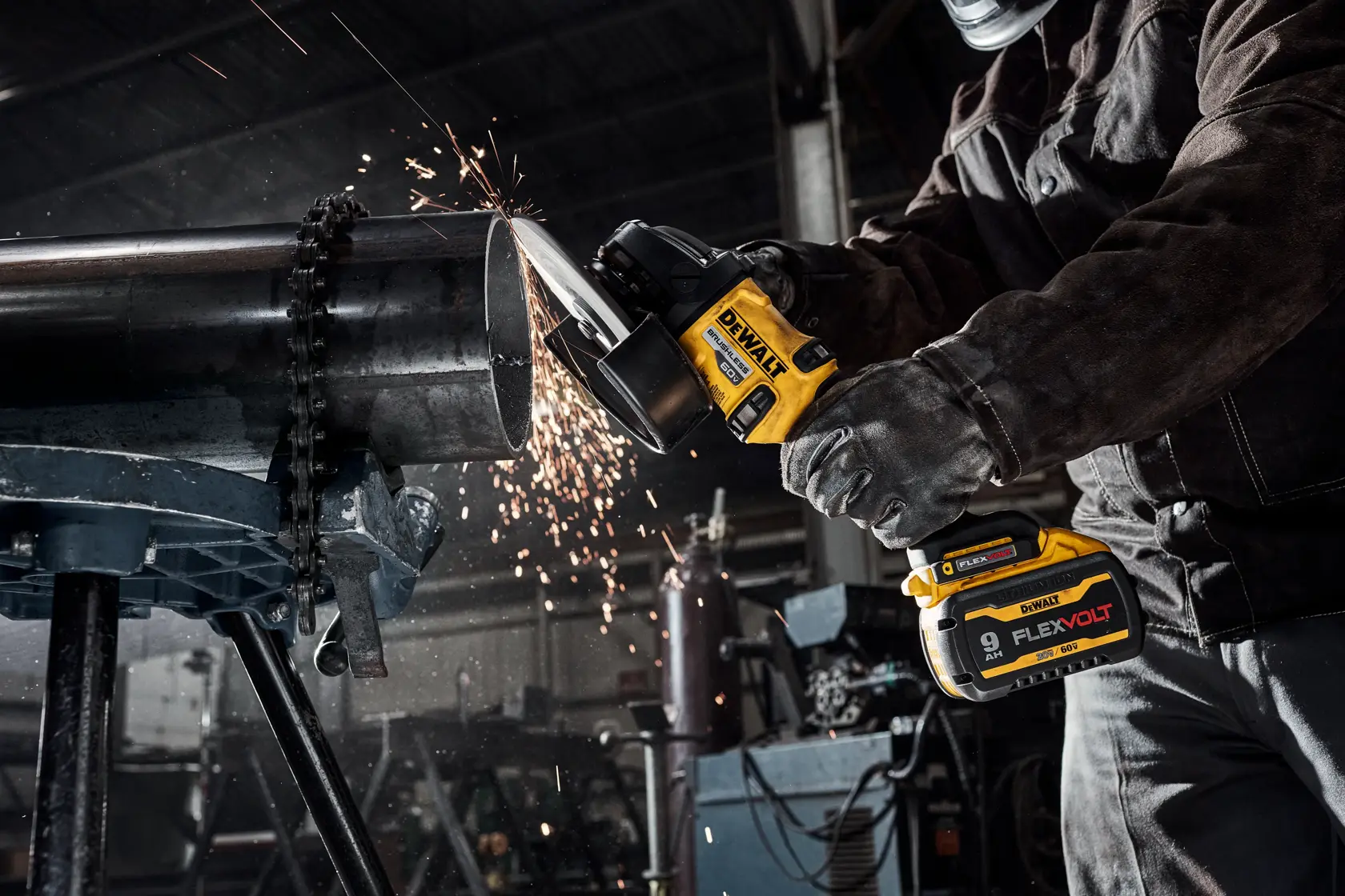 Uma pessoa usando equipamento de proteção utiliza uma esmerilhadeira angular sem fio DEWALT para cortar um grande tubo de metal em uma oficina industrial, com faíscas voando durante o corte.