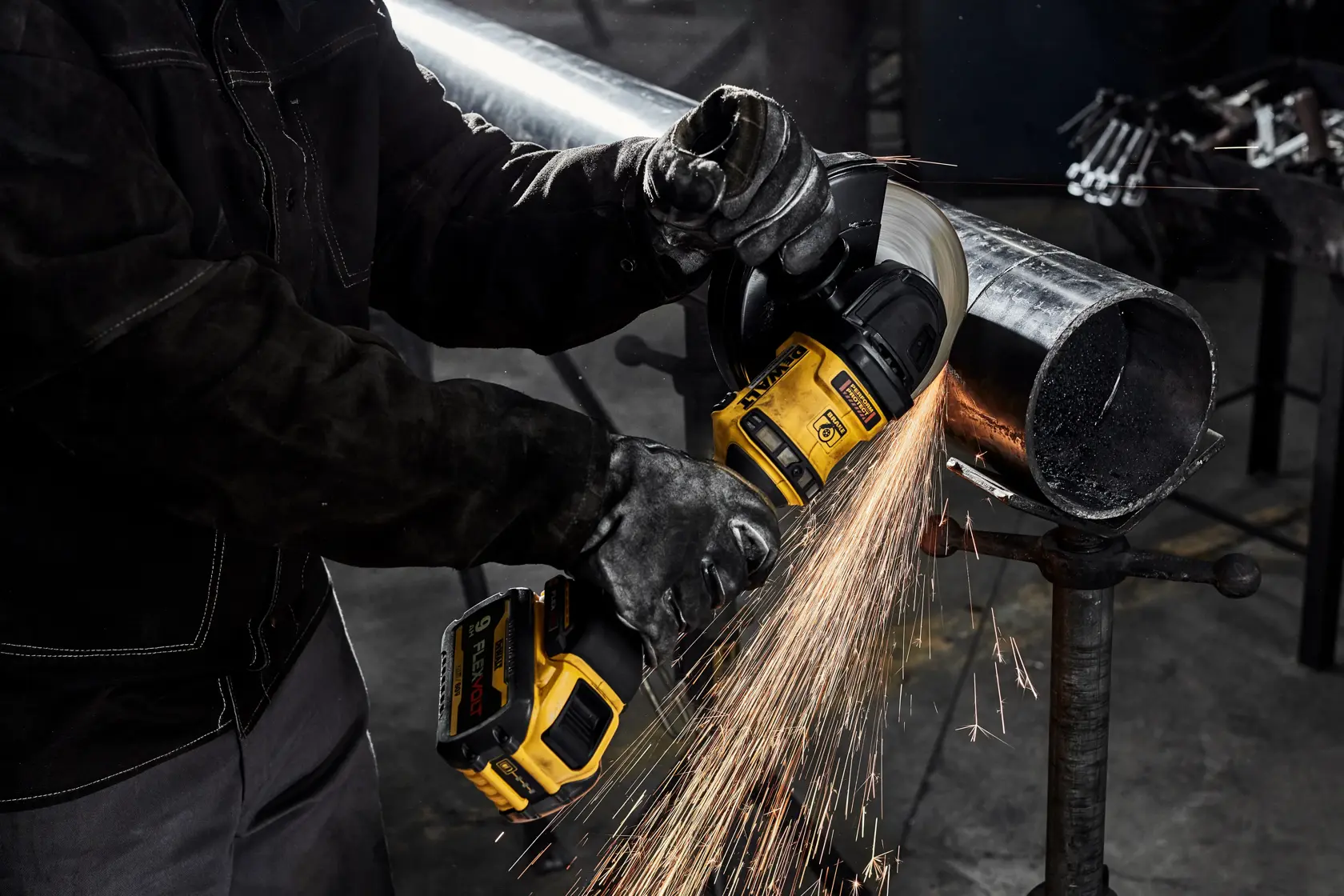 Um trabalhador usando luvas de proteção utiliza uma esmerilhadeira angular sem fio DEWALT para cortar um tubo de metal, gerando faíscas.