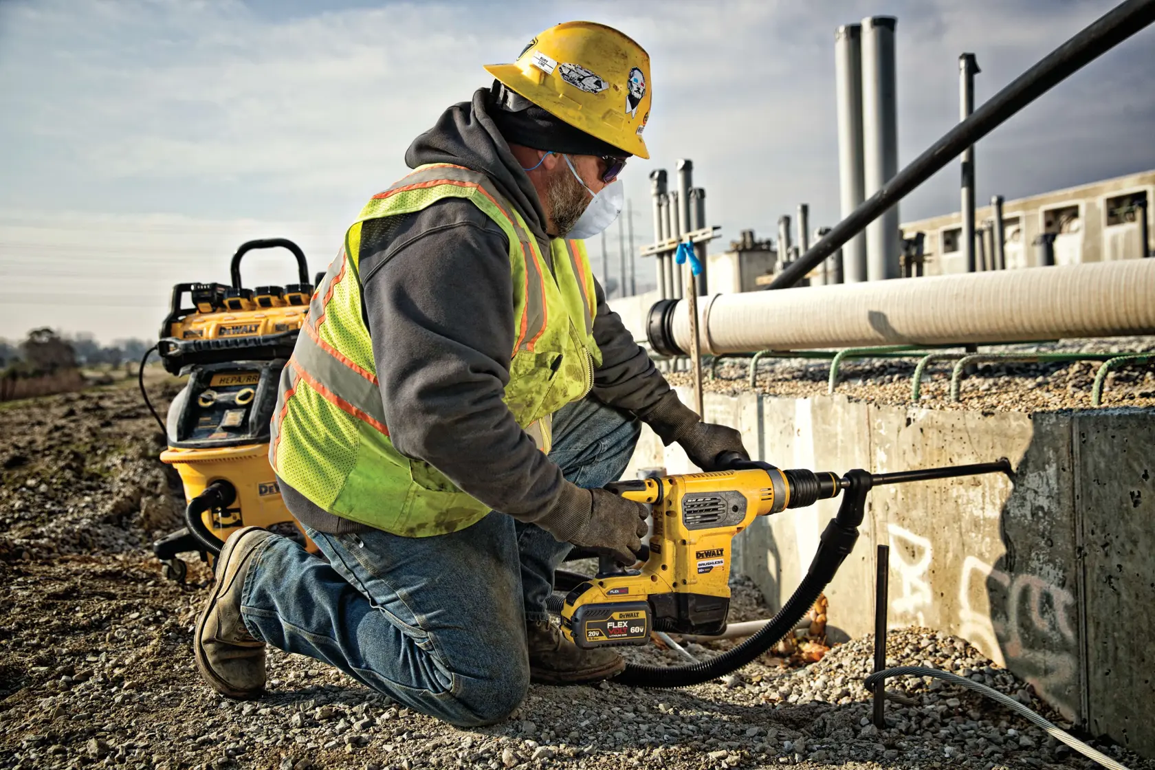 Trabalhador usa martelete DEWALT DCH481X2 em concreto, vestindo capacete e colete de segurança.