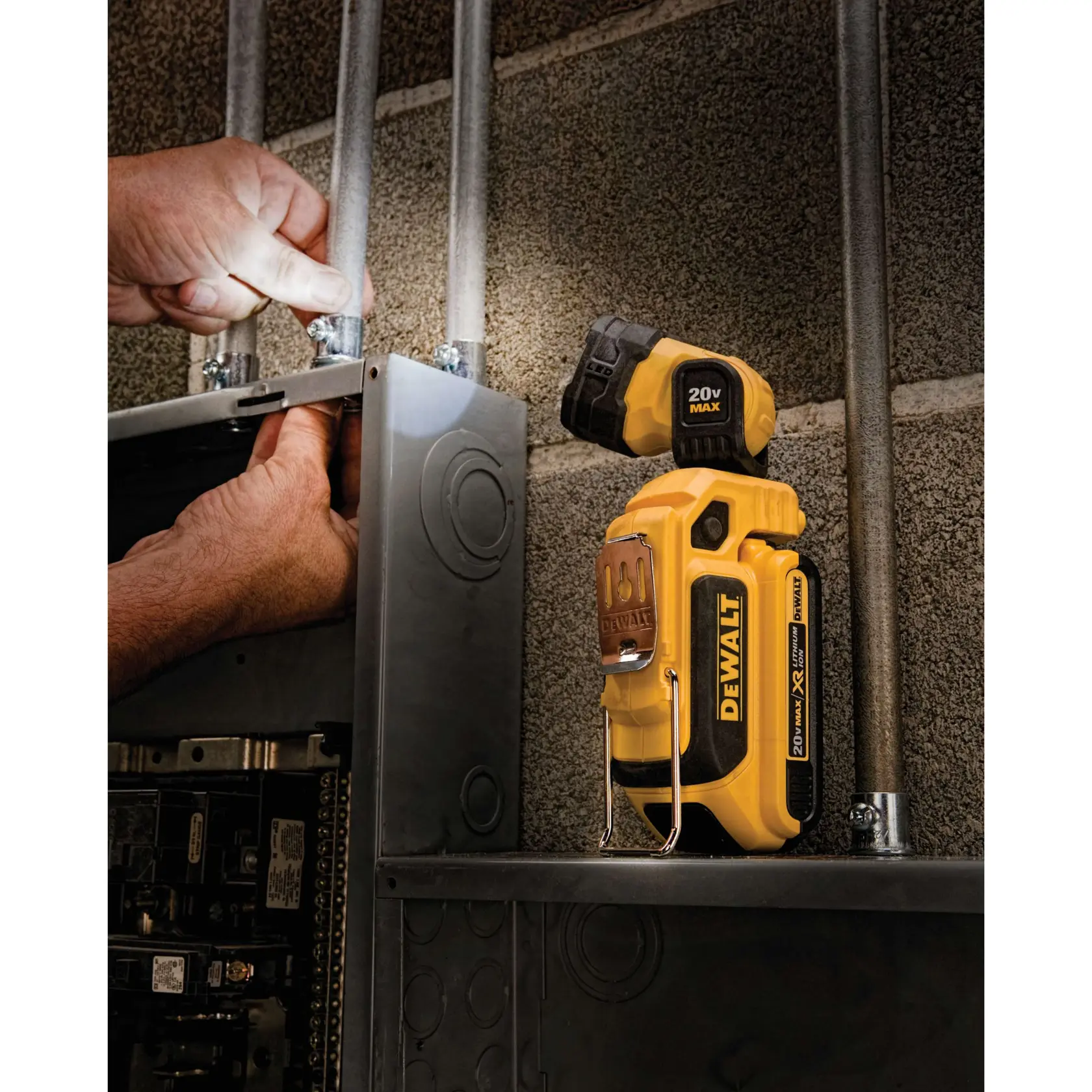 Uma lanterna de trabalho portátil DEWALT modelo DCL044 está iluminando um espaço dentro de um painel elétrico. As mãos de uma pessoa trabalham na fiação, e a luz está direcionada ao painel para fornecer visibilidade.