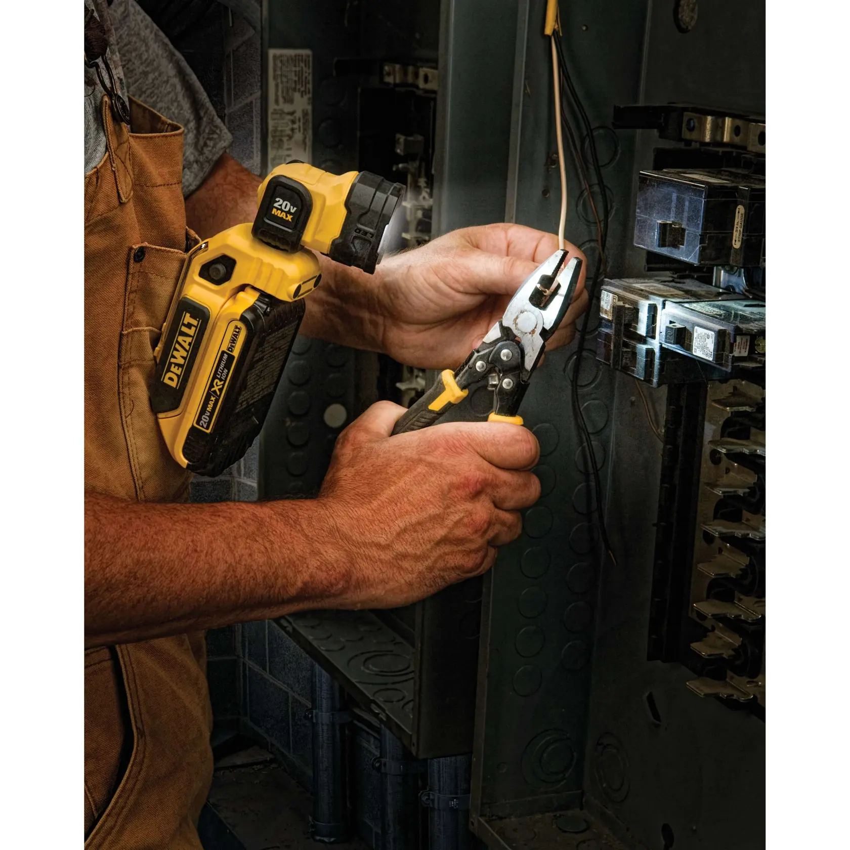Uma pessoa utiliza uma lanterna LED DEWALT DCL044 20V MAX para iluminar um painel elétrico enquanto trabalha com alicates nos fios.