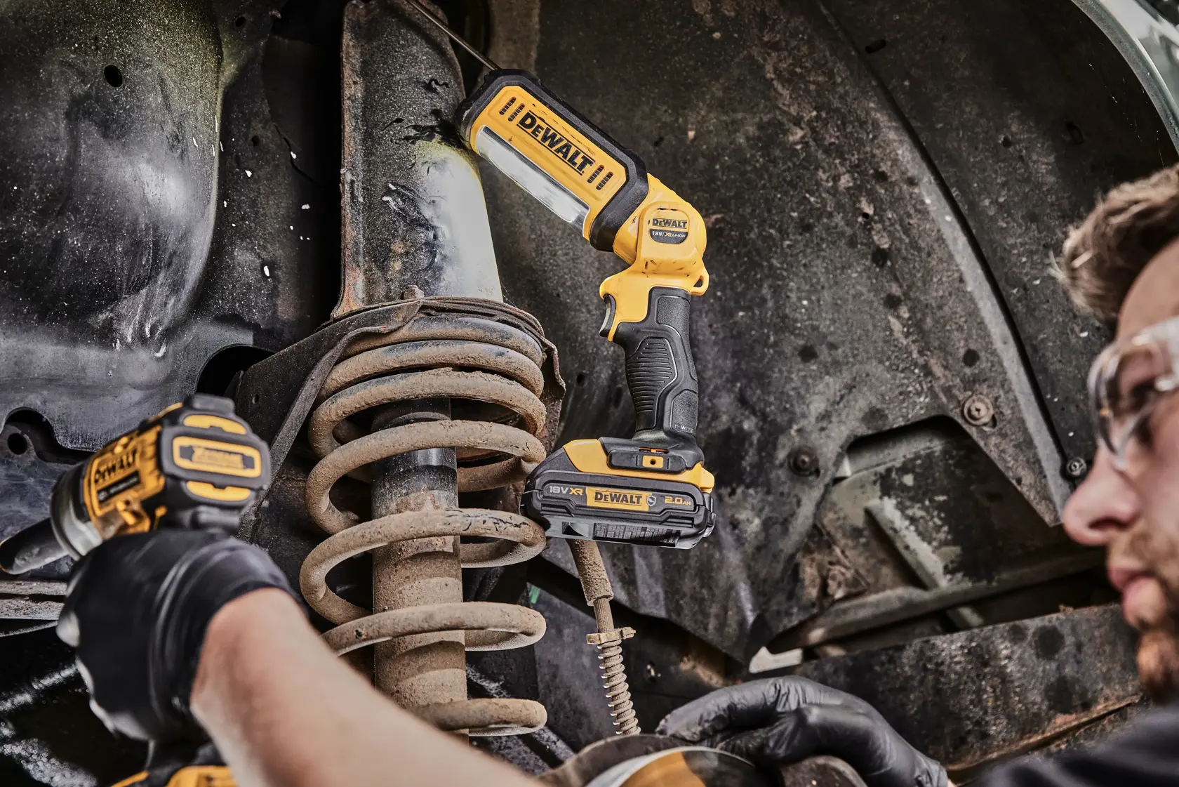 Foto da luz de trabalho DEWALT DCL050 iluminando suspensão de carro sendo reparada, ferramenta amarela visível.