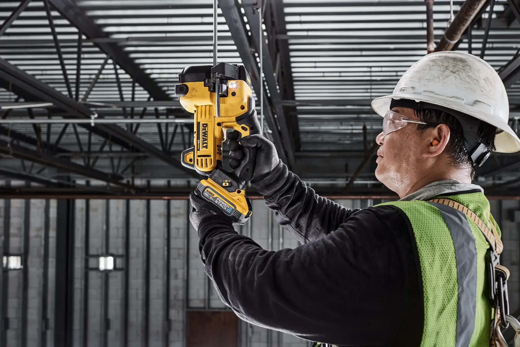 Um trabalhador da construção civil usando capacete e colete de segurança utiliza uma ferramenta DEWALT DCS350B para cortar uma barra de metal em um ambiente industrial.