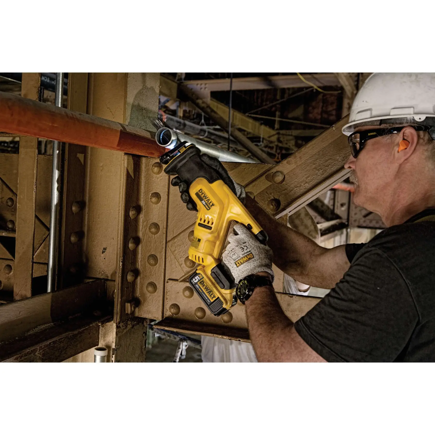 Uma pessoa usando luvas e capacete utiliza uma serra recíproca sem fio DEWALT DCS387B para cortar um tubo de metal em um ambiente industrial.