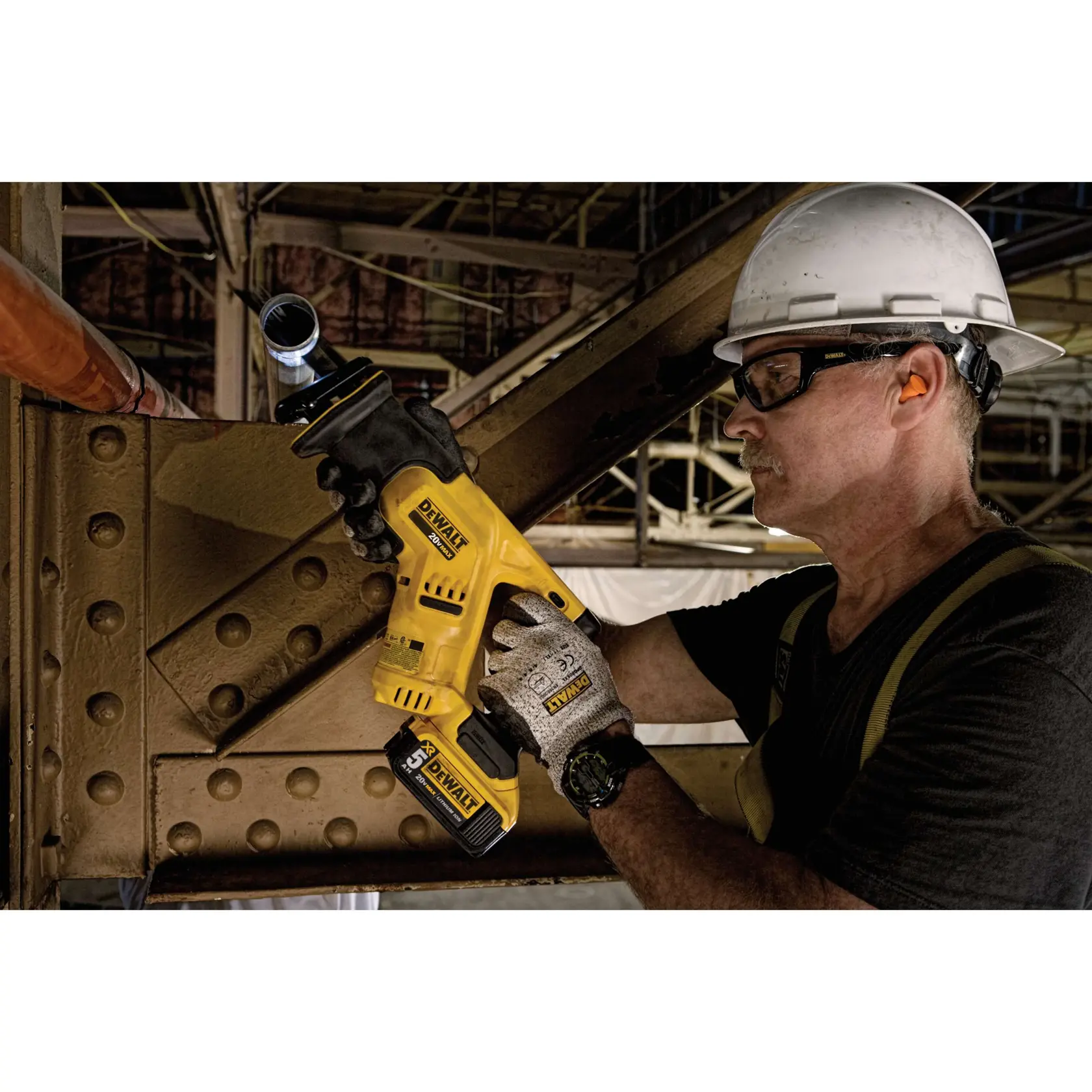Uma pessoa usando capacete e luvas está utilizando uma serra recíproca sem fio amarela da DEWALT para cortar um tubo de metal em um local de construção industrial. O rosto da pessoa está desfocado para manter a privacidade.