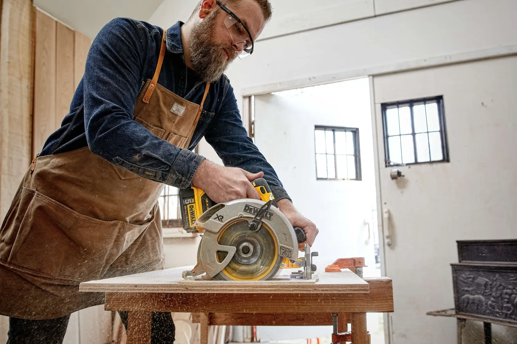Pessoa usando uma serra circular DEWALT DCS570B para cortar madeira em uma bancada de oficina.
