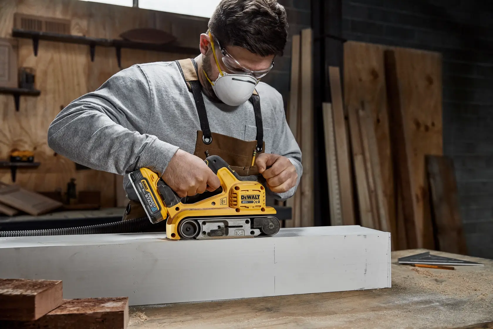 Imagem em close-up de uma ferramenta elétrica DEWALT 20V XR brushless, especificamente uma lixadeira de cinta, mostrando um mecanismo de liberação rápida para fácil troca da cinta de lixa. O texto em francês destaca o rápido substituição da cinta e troca simples do papel abrasivo.