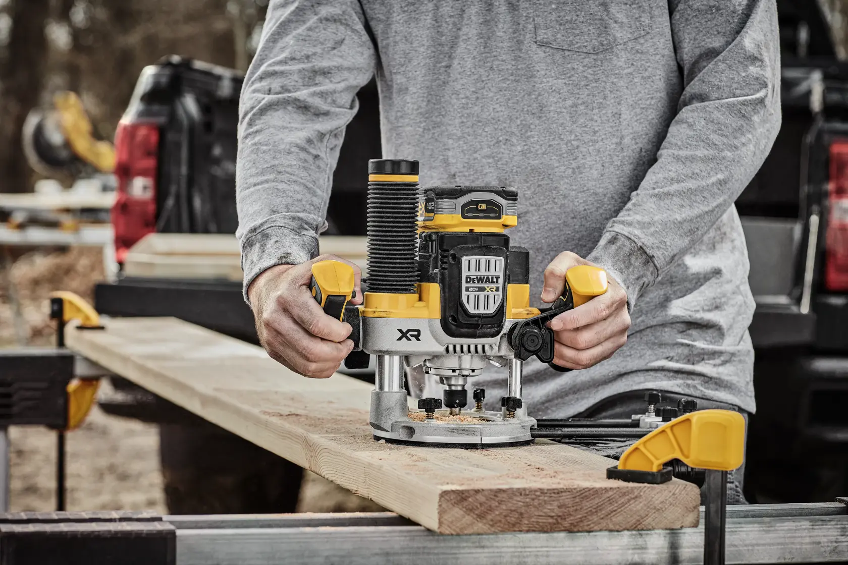 Uma pessoa usando uma tupia sem fio DEWALT 20V MAX para trabalhar em uma peça de madeira, com um acessório de extração de pó conectado. A tupia está destacada e o texto diz: 'Nossa tupia sem fio 20V MAX* mais potente.' Bateria vendida separadamente.