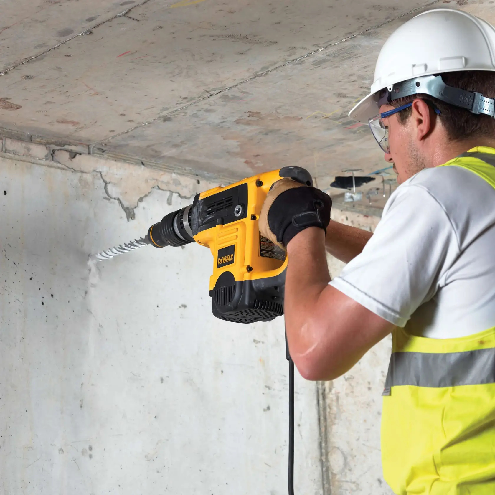 Trabalhador perfura parede de concreto usando DEWALT DT9445, com capacete e equipamento de segurança.
