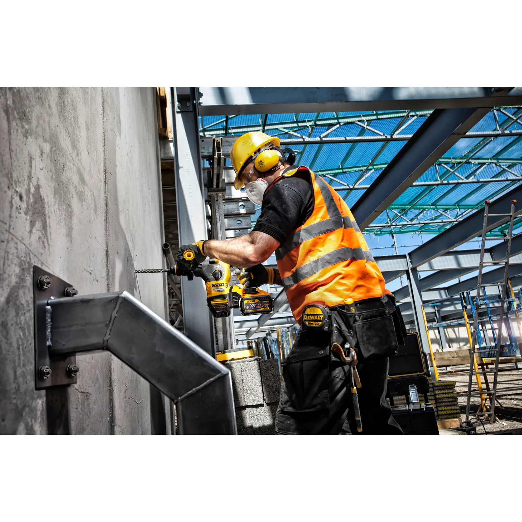 Trabalhador perfura parede de concreto com ferramenta DEWALT na obra, usando equipamentos de segurança e colete laranja.
