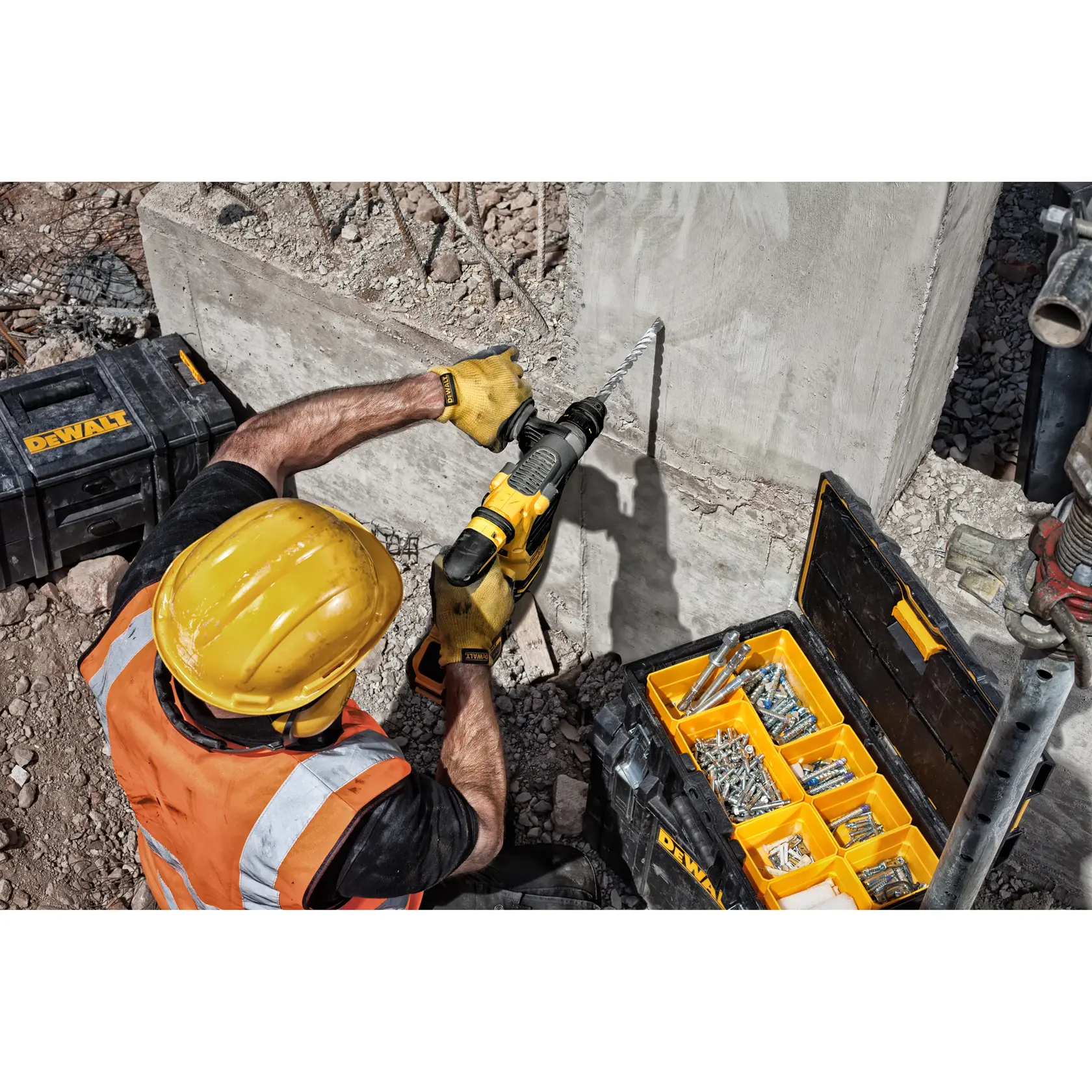 Trabalhador fura concreto com ferramenta DeWalt, cercado por caixas de ferramentas na obra.