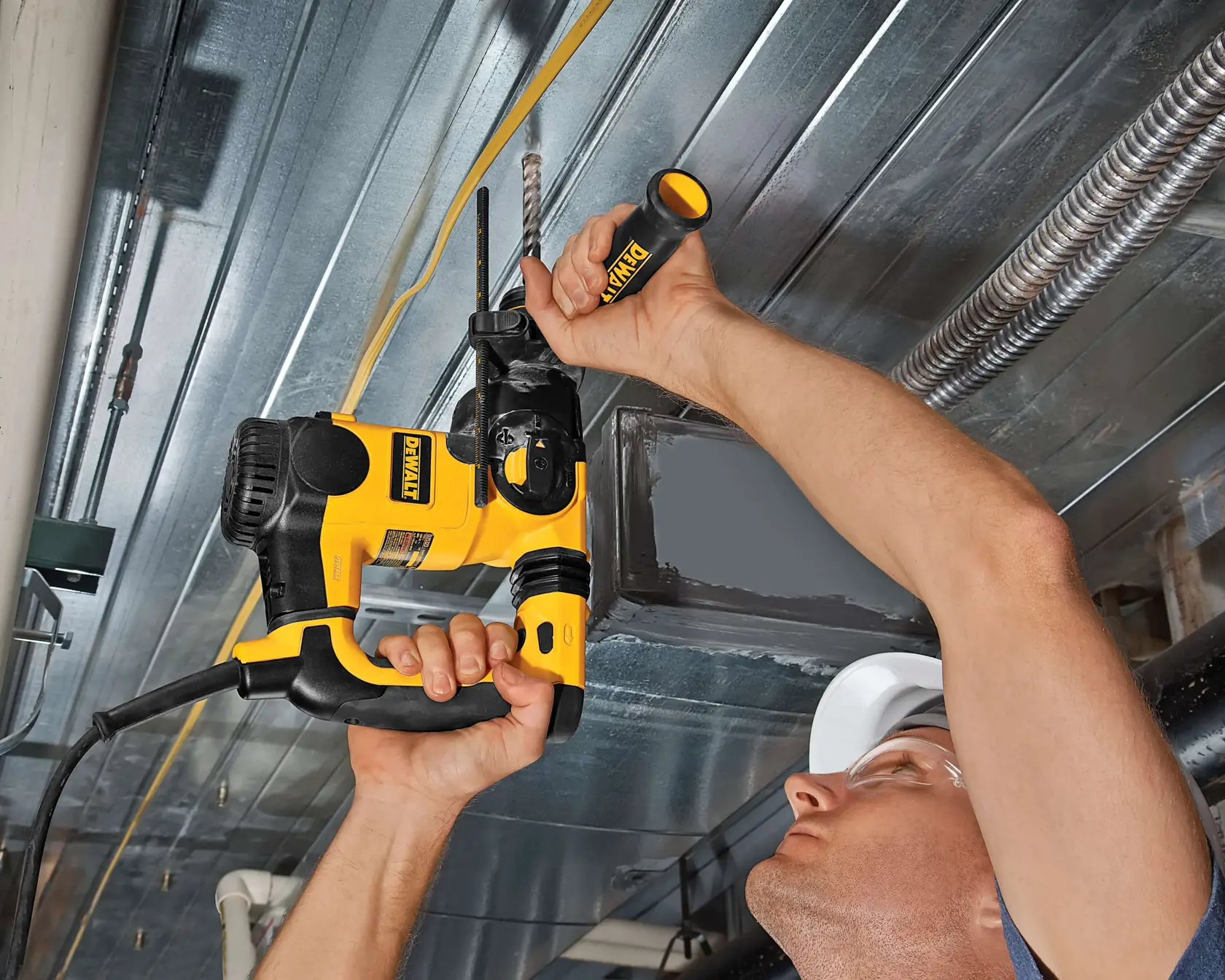 Pessoa usa martelo rotativo DEWALT para perfurar teto metálico, segurando a ferramenta com ambas as mãos.