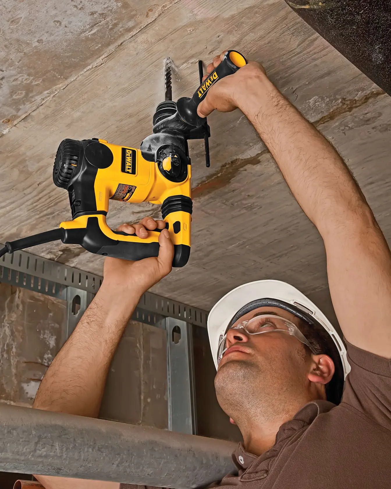 Pessoa usando uma furadeira DEWALT amarela para perfurar teto de concreto, usando capacete de segurança.