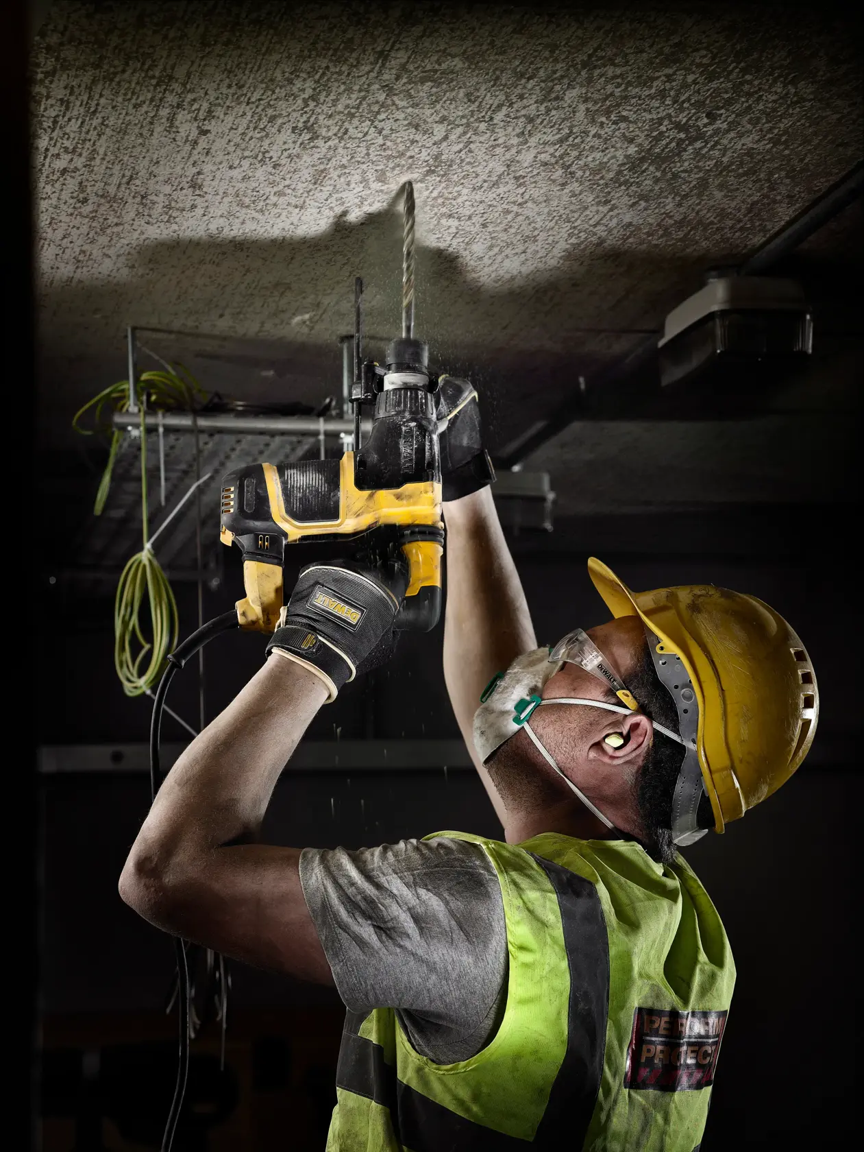 Trabalhador com EPI usa furadeira DEWALT para perfurar o teto em obra.
