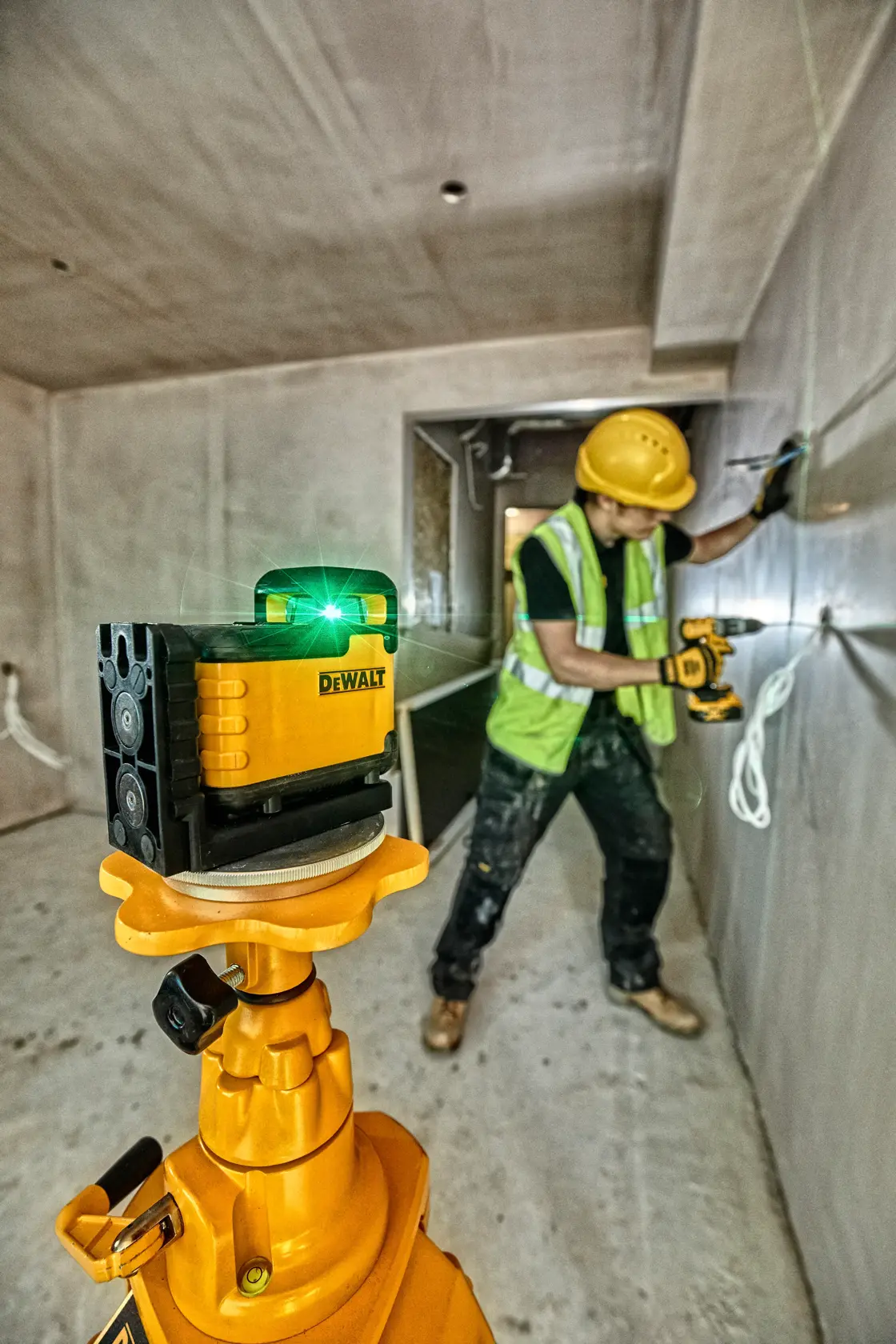 Um nível a laser DEWALT montado em um tripé está posicionado em primeiro plano enquanto uma pessoa instala armários de madeira em uma parede de um cômodo. A linha do laser ajuda a garantir um alinhamento preciso durante a instalação.
