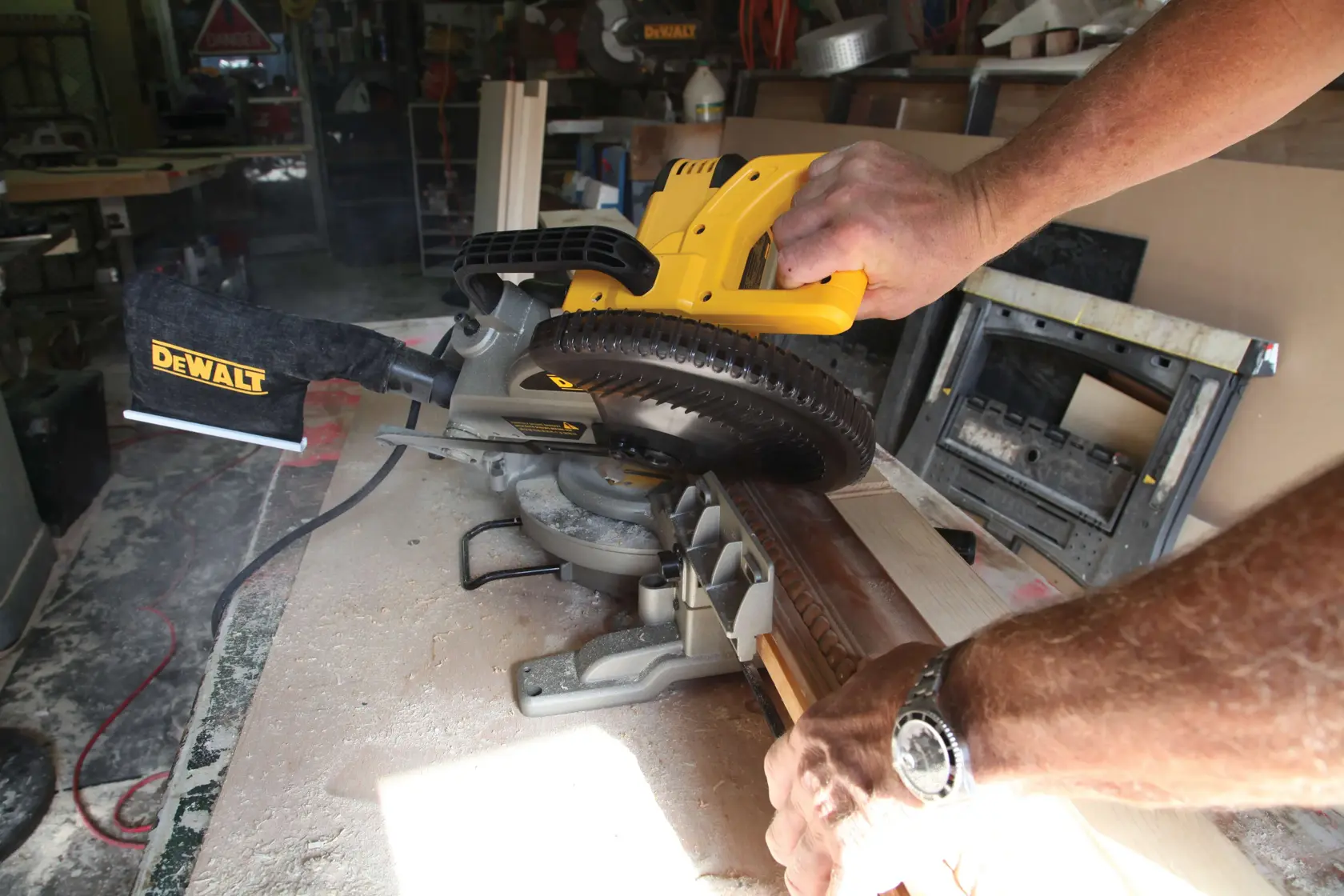 Uma pessoa usa uma serra de esquadria DEWALT para cortar um pedaço de madeira em uma oficina.