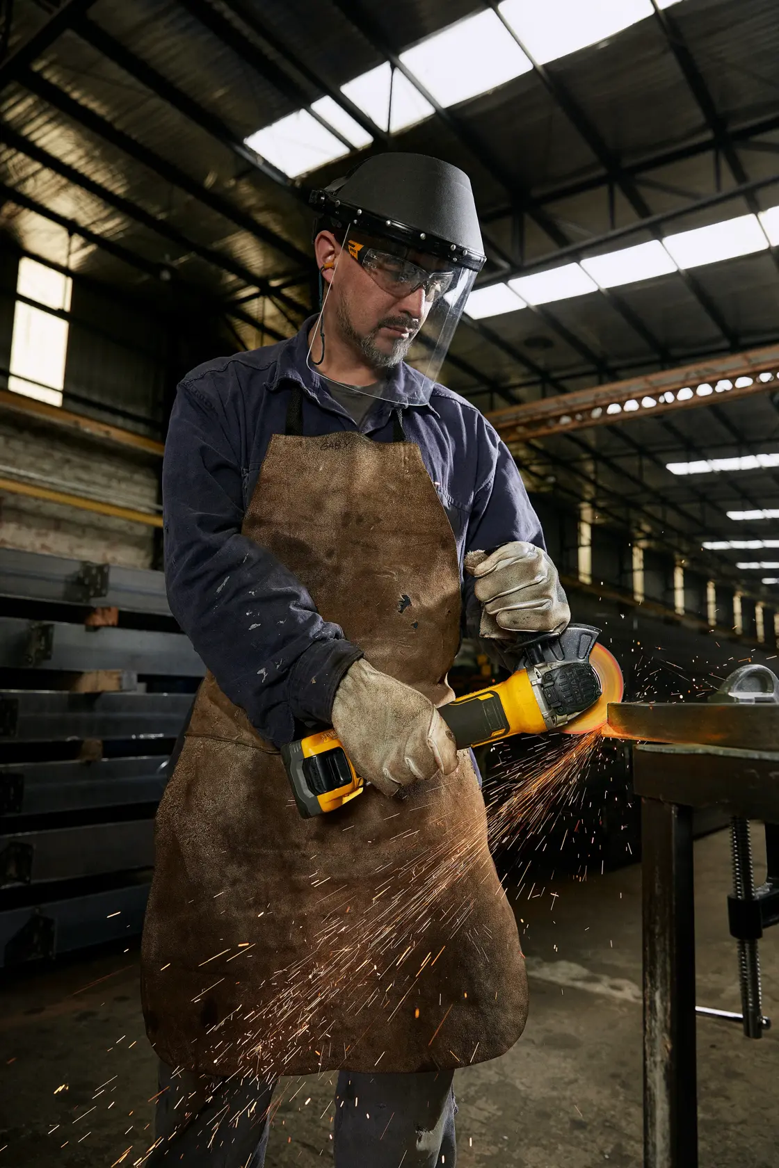 Trabalhador usa esmeril DEWALT com proteção, faíscas voando em ambiente industrial.