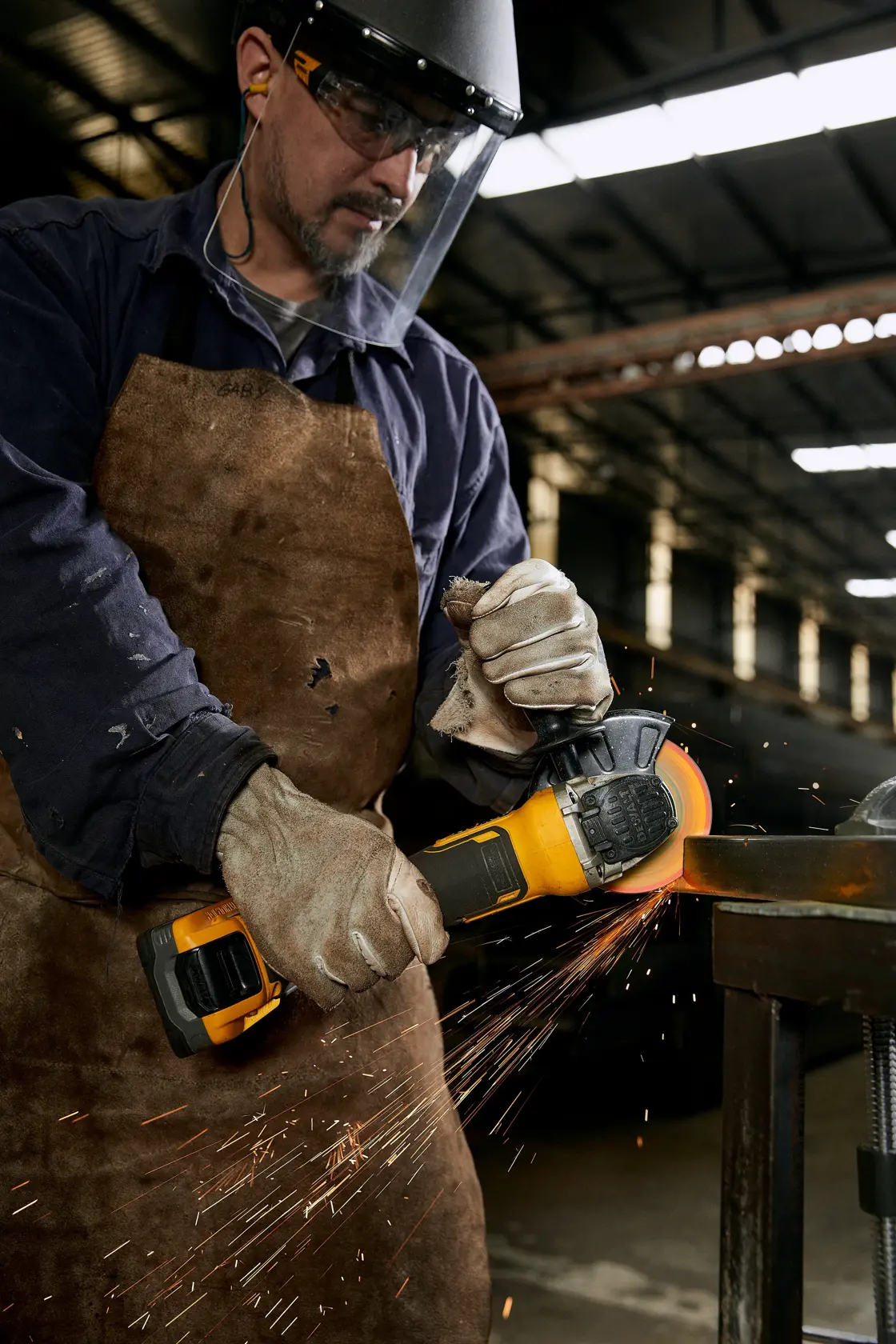 Operário usa esmerilhadeira DEWALT com luvas e avental, gerando faíscas em ambiente industrial.