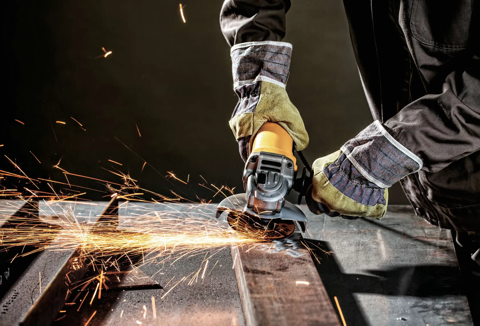 Fotografia da DEWALT DWE4118 esmerilhadeira angular em uso, cortando metal e faiscas, operador com luvas.