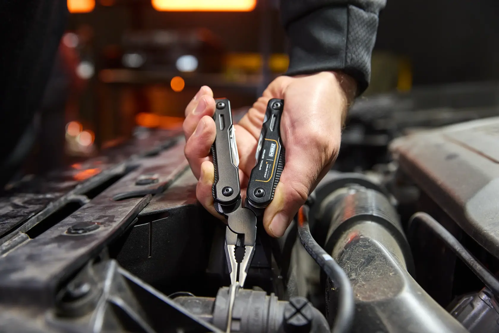 Mão usa alicate multitool DEWALT para segurar um fio no compartimento do motor.