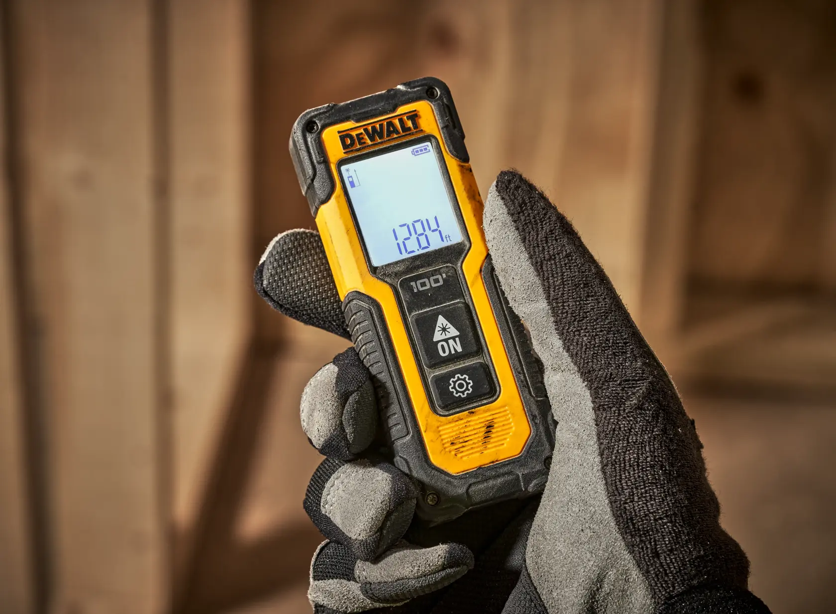 Un medidor de distancia digital láser portátil de color amarillo y negro con una pantalla que muestra una lectura de 128.4 pies, marca DEWALT. Tiene varios botones para su funcionamiento y un diseño robusto.