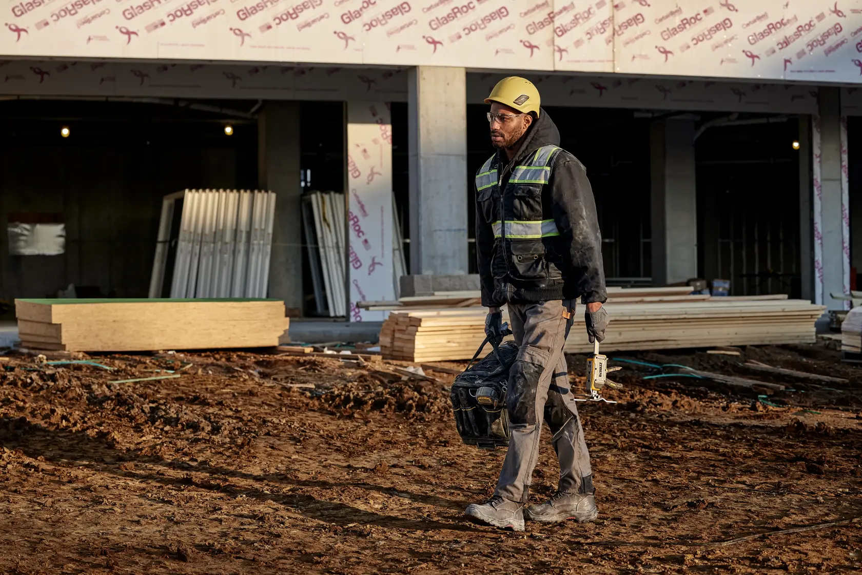 Una herramienta step-to-lift DEWALT utilizada para levantar una puerta sin manos usando una asa reforzada, operada con el pie de una persona. La herramienta está sujetada a la base de la puerta, permitiendo un levantamiento fácil y sin manos en un entorno de construcción.